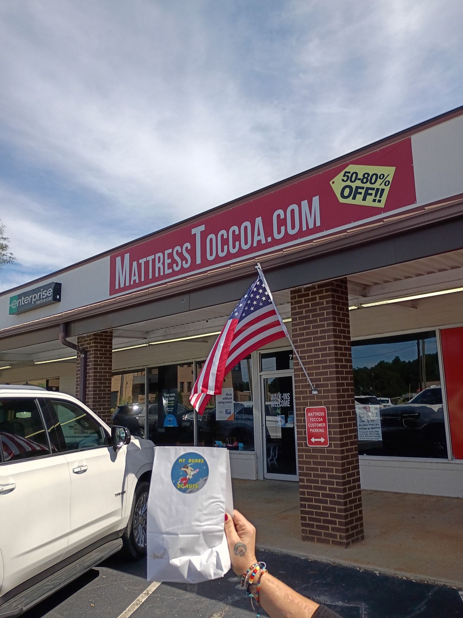 Exterior of MattressToccoa.com store with American flag and person holding a white bag.