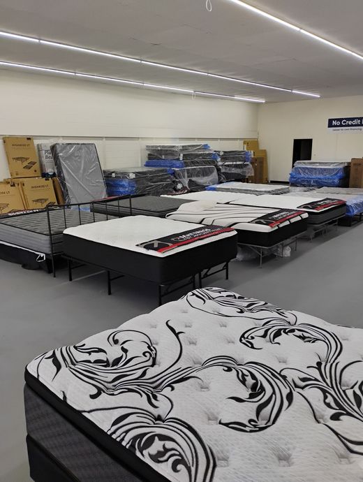 A showroom filled with mattresses, featuring patterned and solid-colored designs. Gray floor, bright lighting.