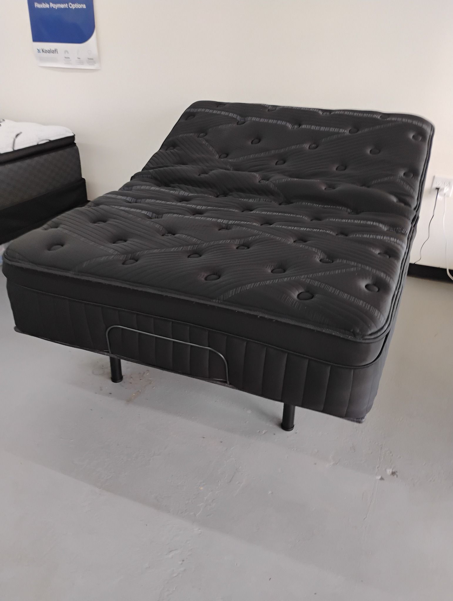 Black adjustable bed on metal legs in a store setting.