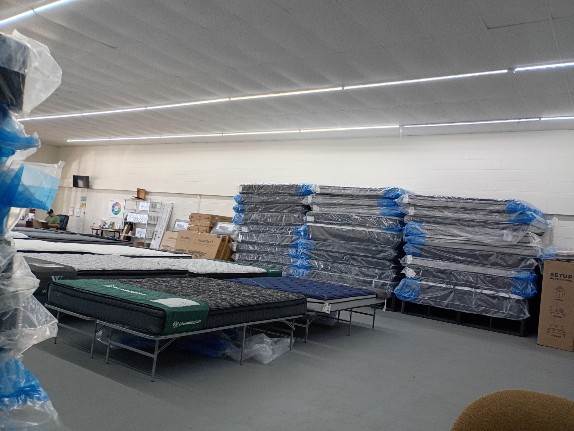 Warehouse with stacks of wrapped mattresses and beds.