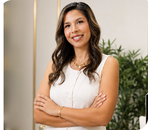 Woman in white sleeveless top, smiling with arms crossed in a bright office setting.