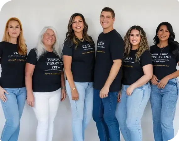 Five people in matching dark shirts and jeans posing against a white wall
