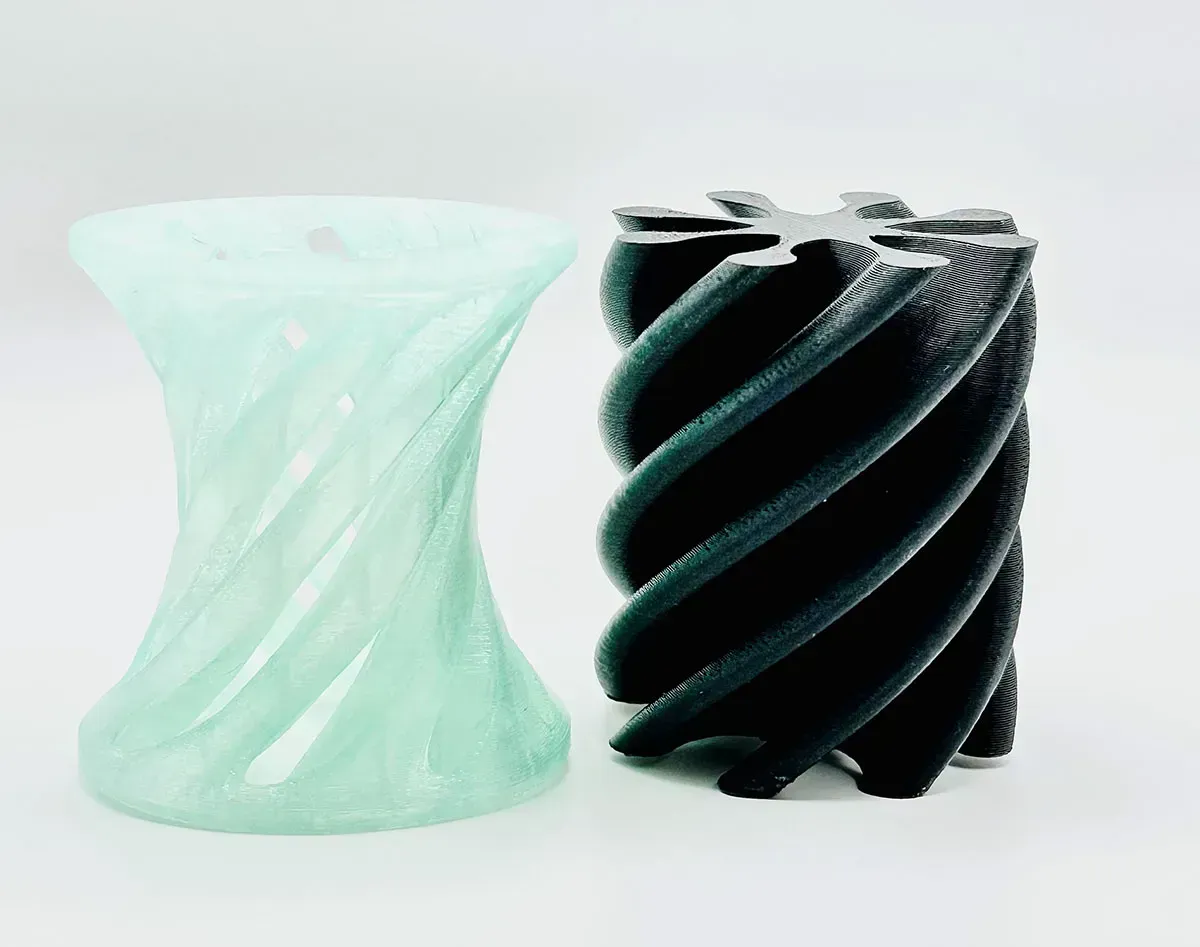 Two 3D-printed cylindrical vases, one mint green and one black with spiral ridges, on a white background
