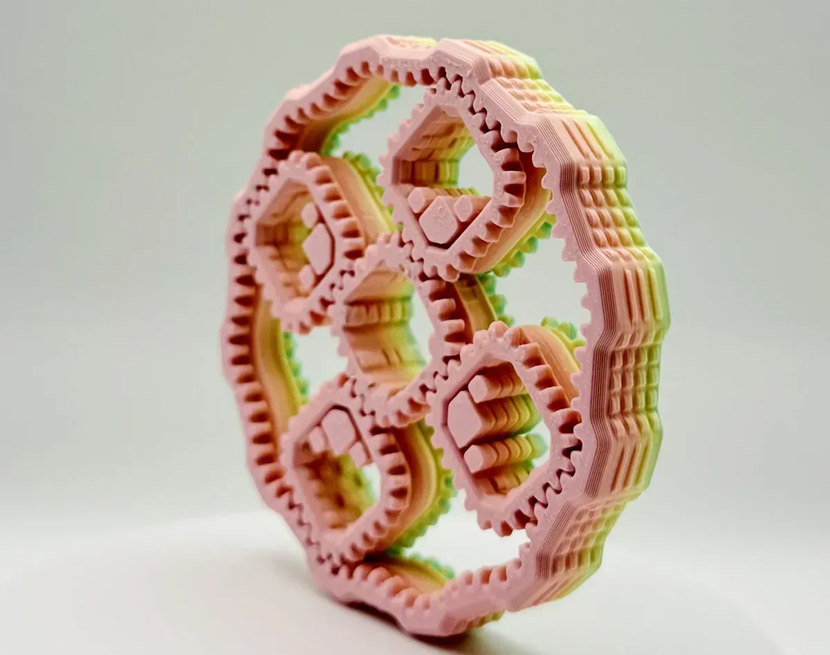 Pink and green 3D-printed decorative ring with hexagonal cutouts on a white background