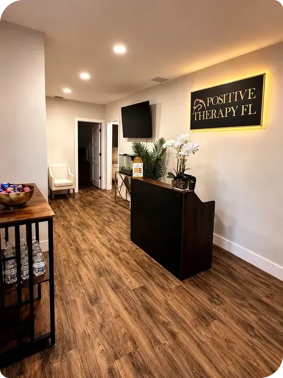 Modern therapy office with wood flooring, black sign, TV, plants, and reception desk