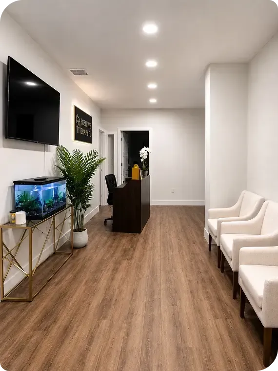 Modern waiting room with white chairs, wall TV, fish tank, wood floors, and a reception desk