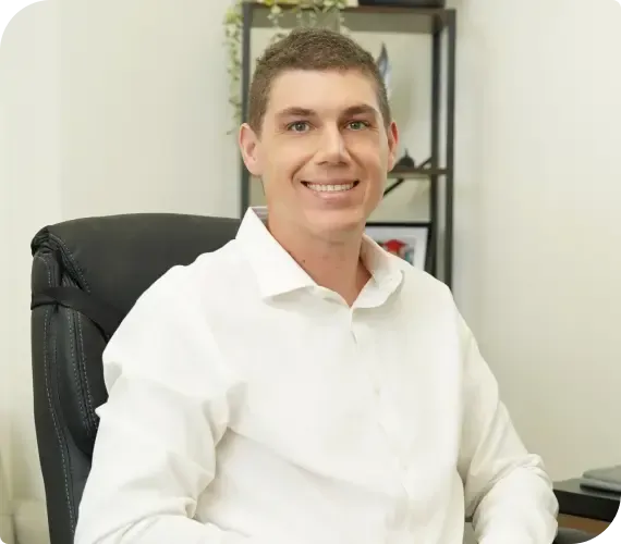 Smiling person in a white shirt seated at a desk in an office chair