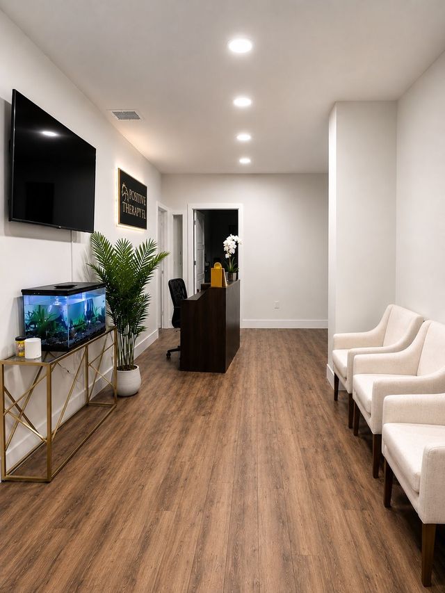 Modern waiting room with white chairs, wood floors, wall-mounted TV, aquarium, and reception desk.