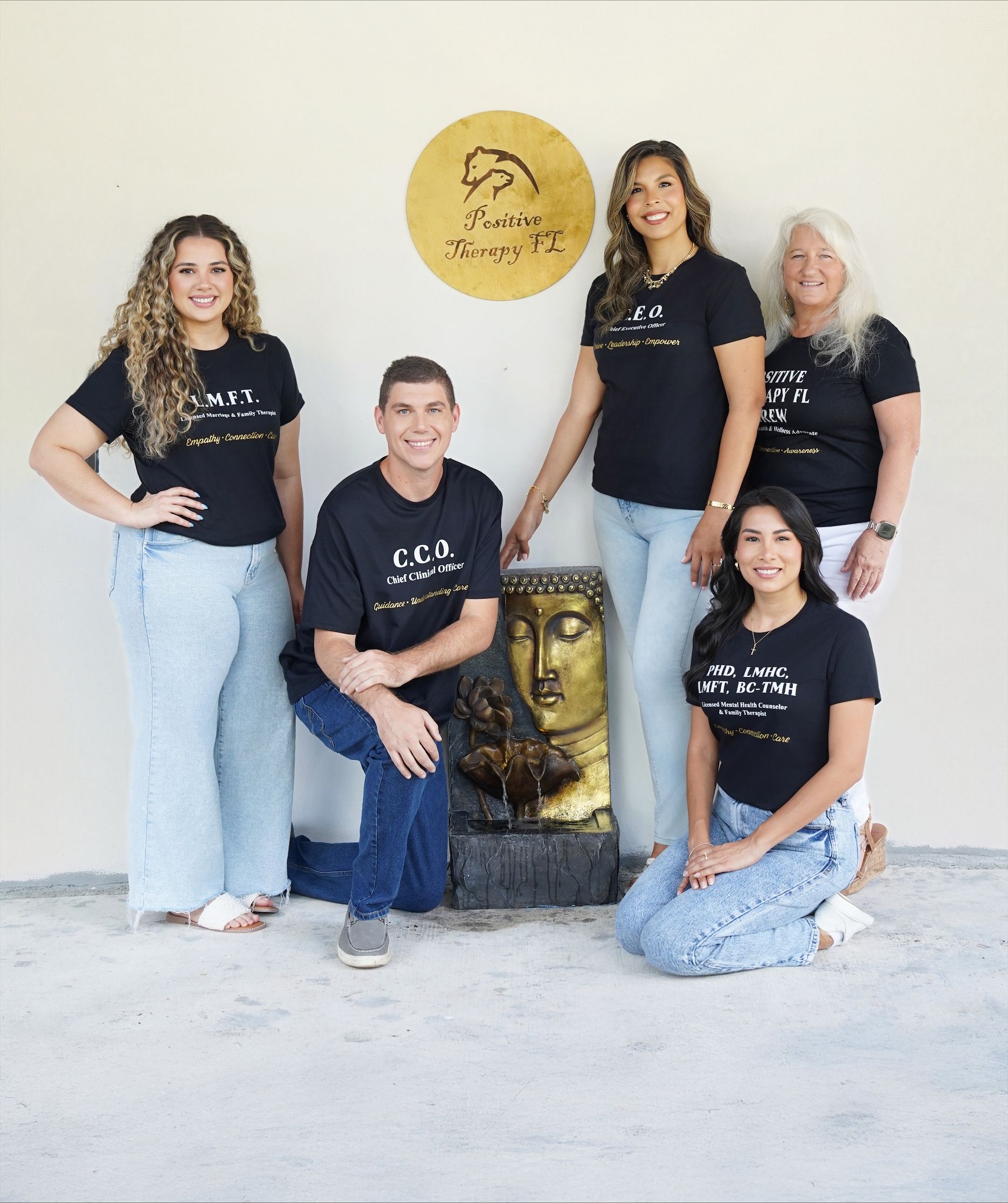 Five people pose indoors by a gold Buddha-style wall decoration.