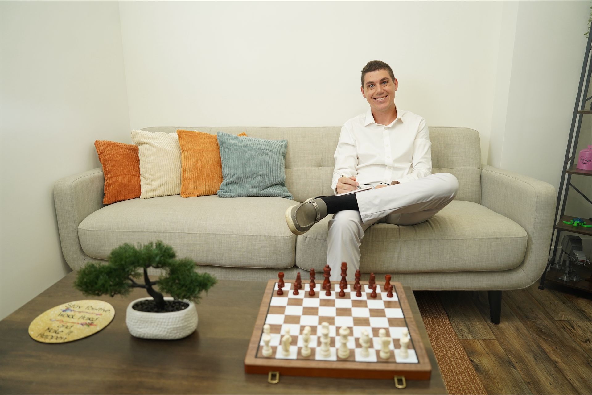 Person sitting on a couch beside a chessboard on a coffee table in a bright living room