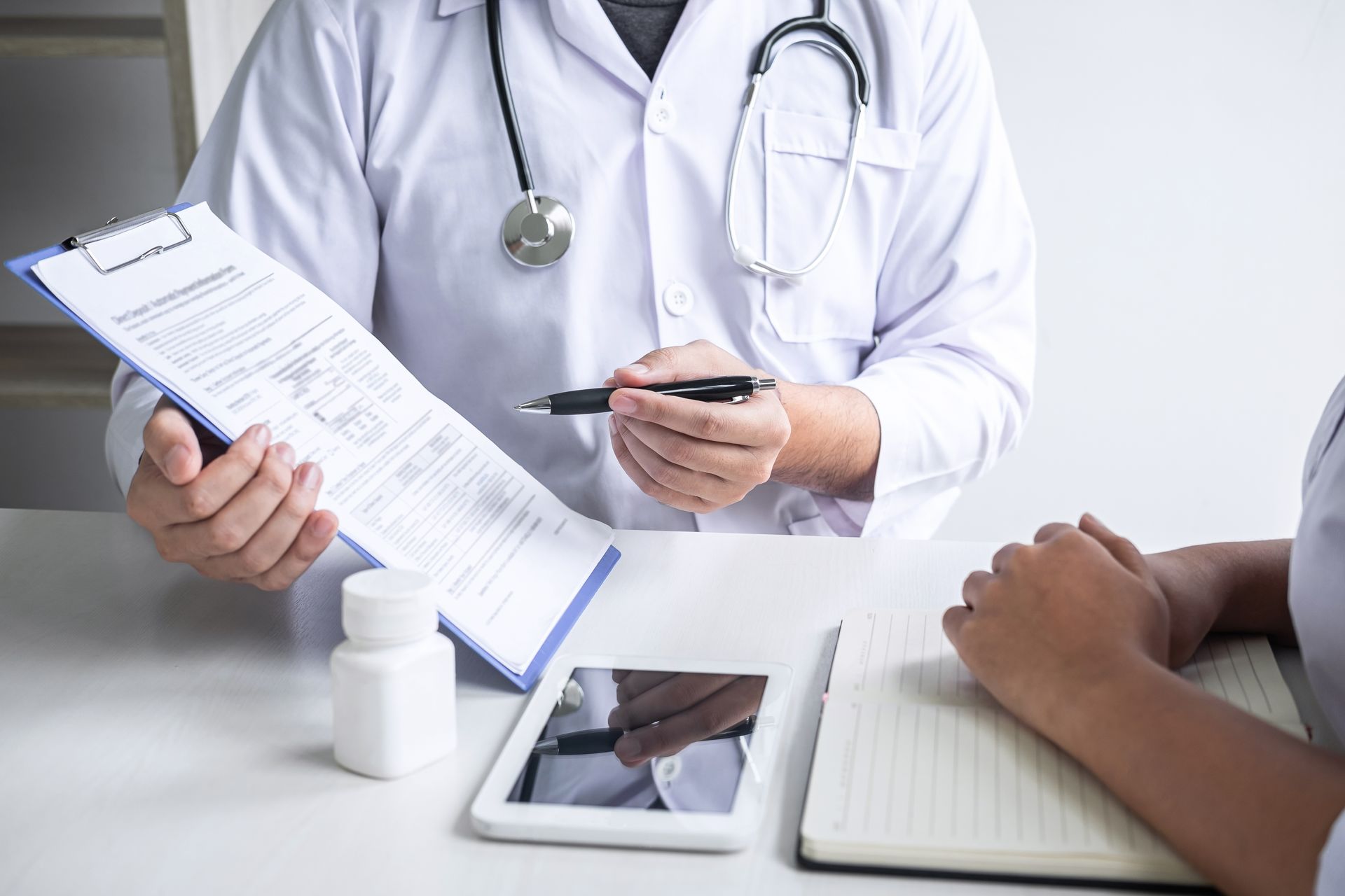Doctor reviewing paperwork with a patient beside a tablet on a desk