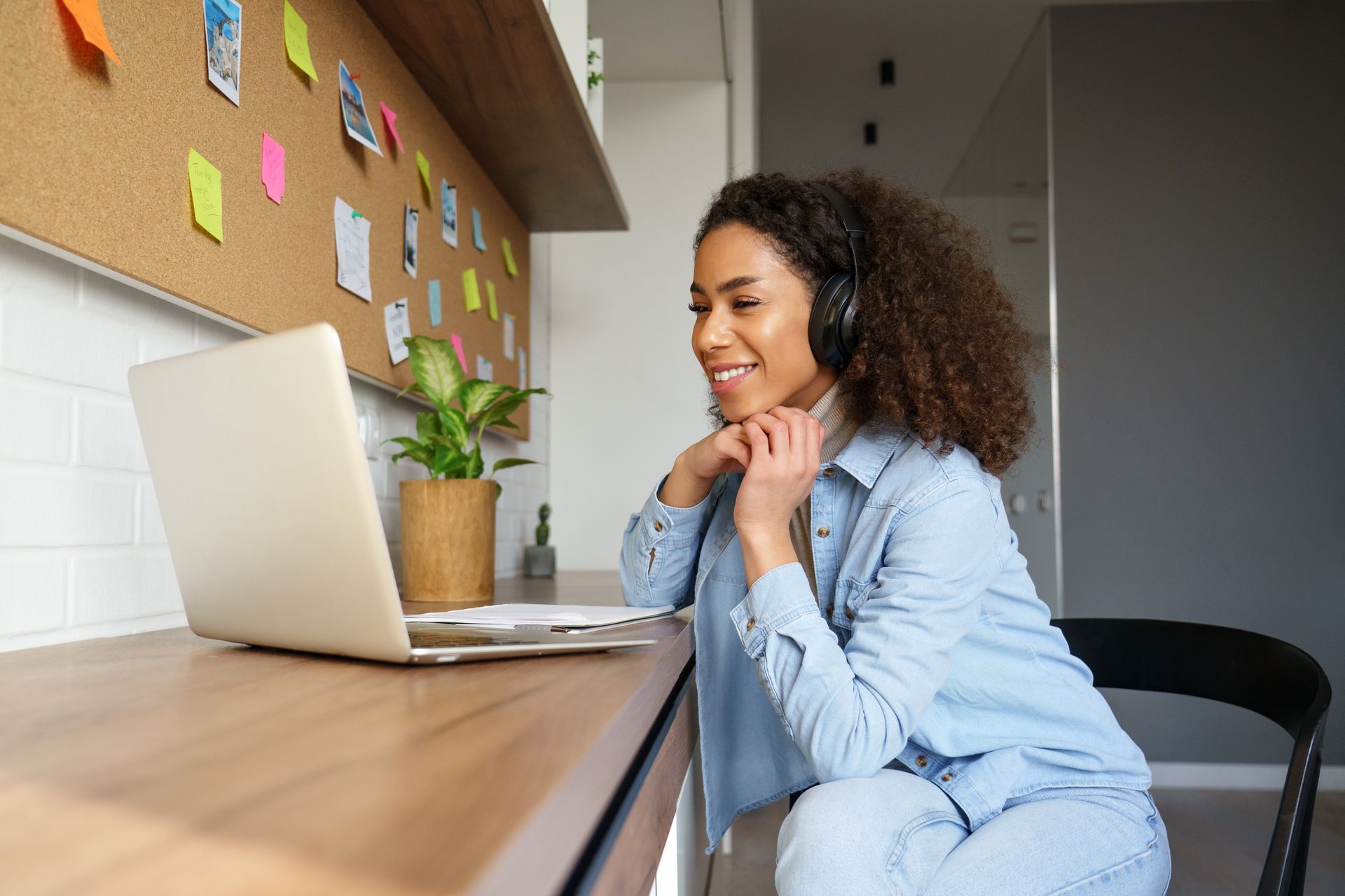 Smiling person using a laptop at a desk with sticky notes and a potted plant nearby