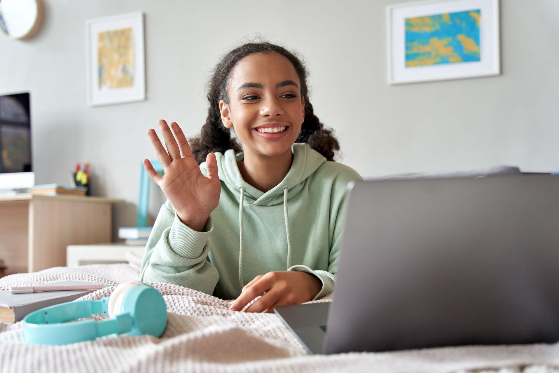 Smiling person waving during a video call at a laptop in a bright bedroom