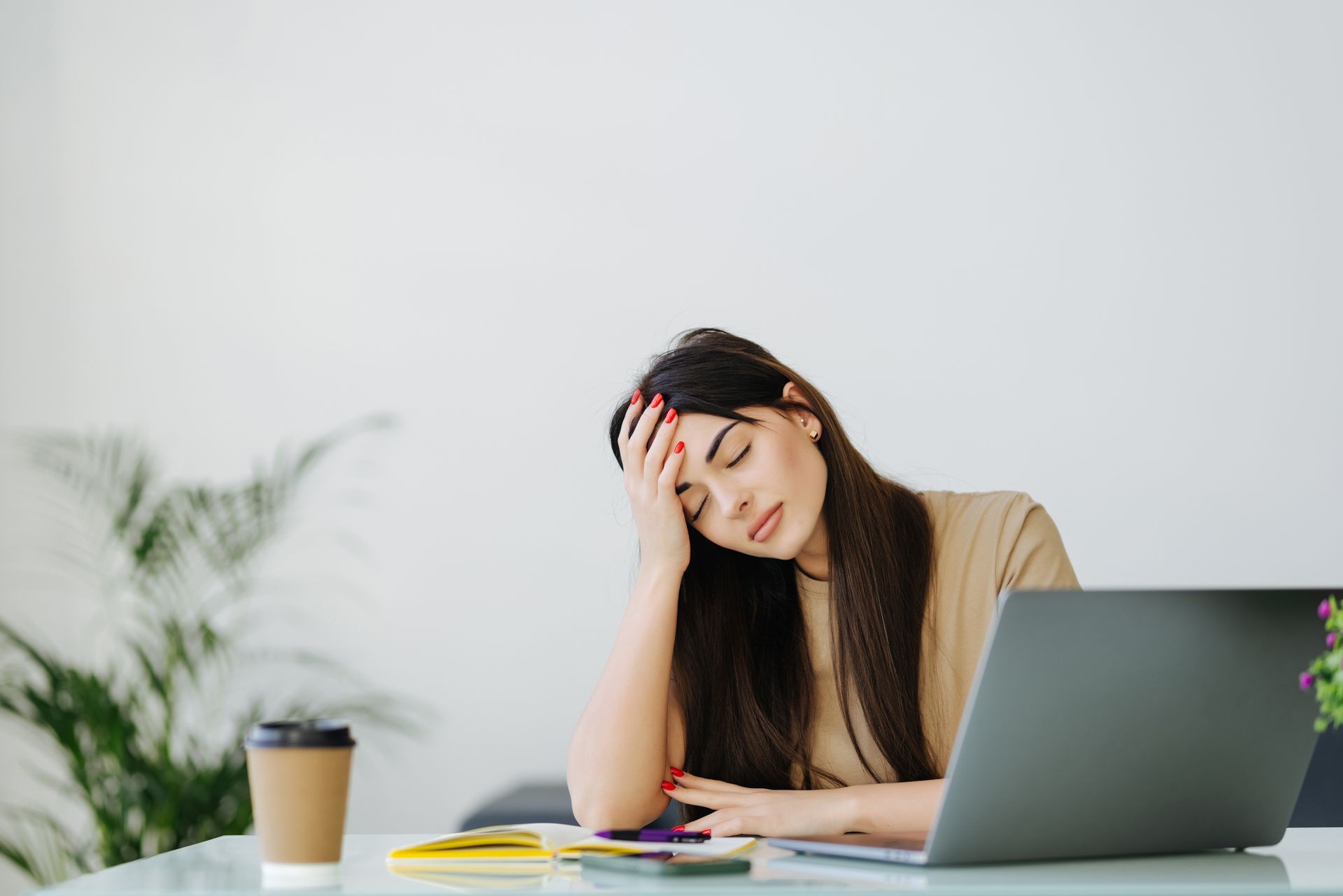 Woman holding her forehead while working on a laptop at a desk, looking stressed