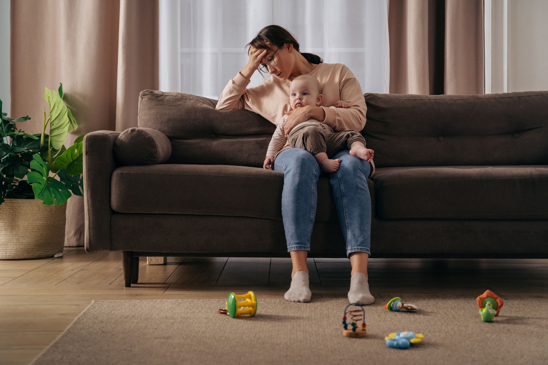 Adult sitting on a couch with a child on their lap in a living room, toys scattered on the floor.