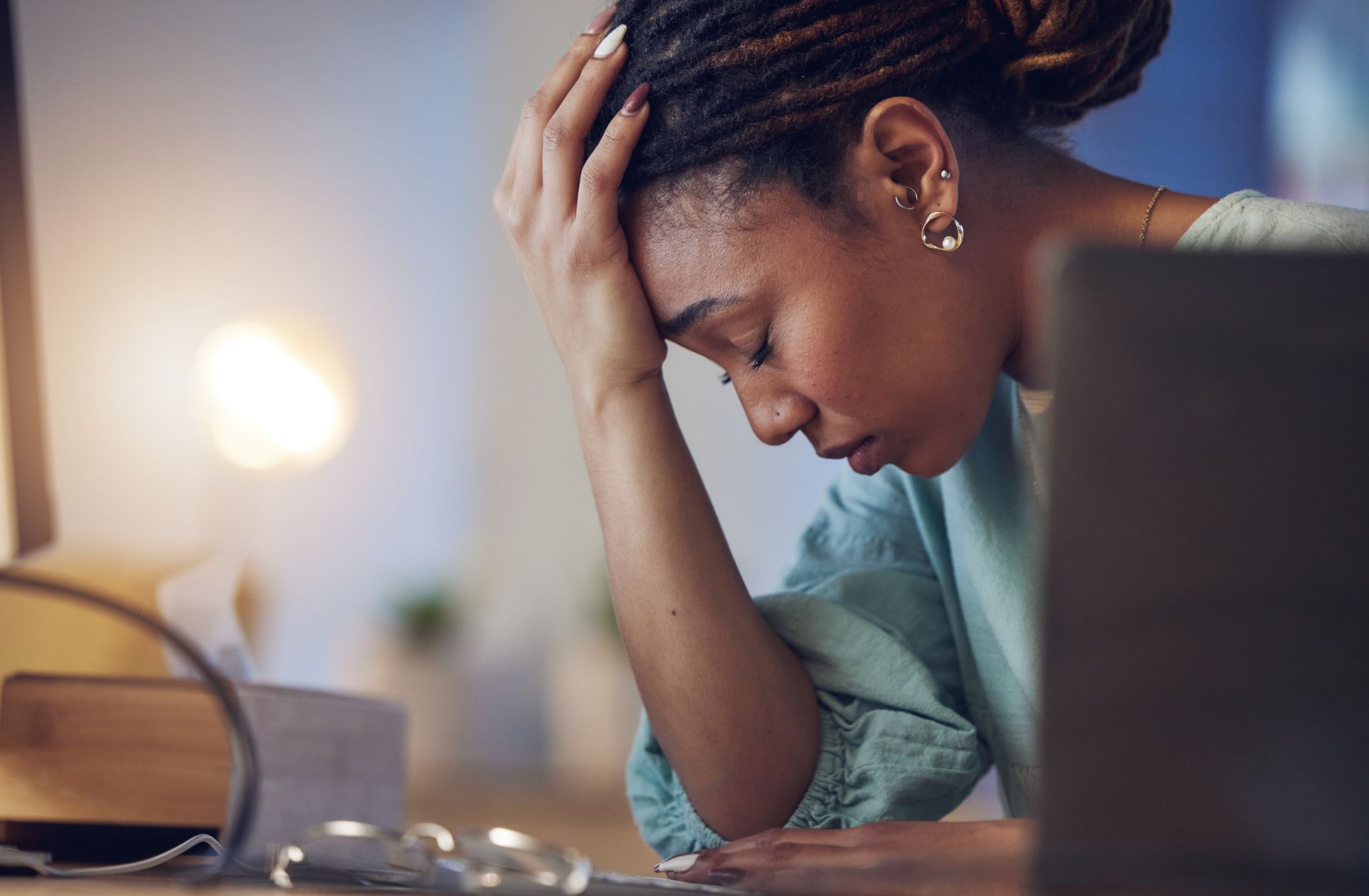 Person resting head on hand while looking at a laptop in a dimly lit room