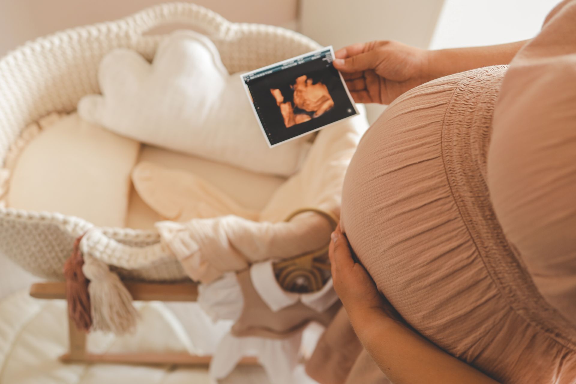 Pregnant person holding an ultrasound photo beside a baby bassinet