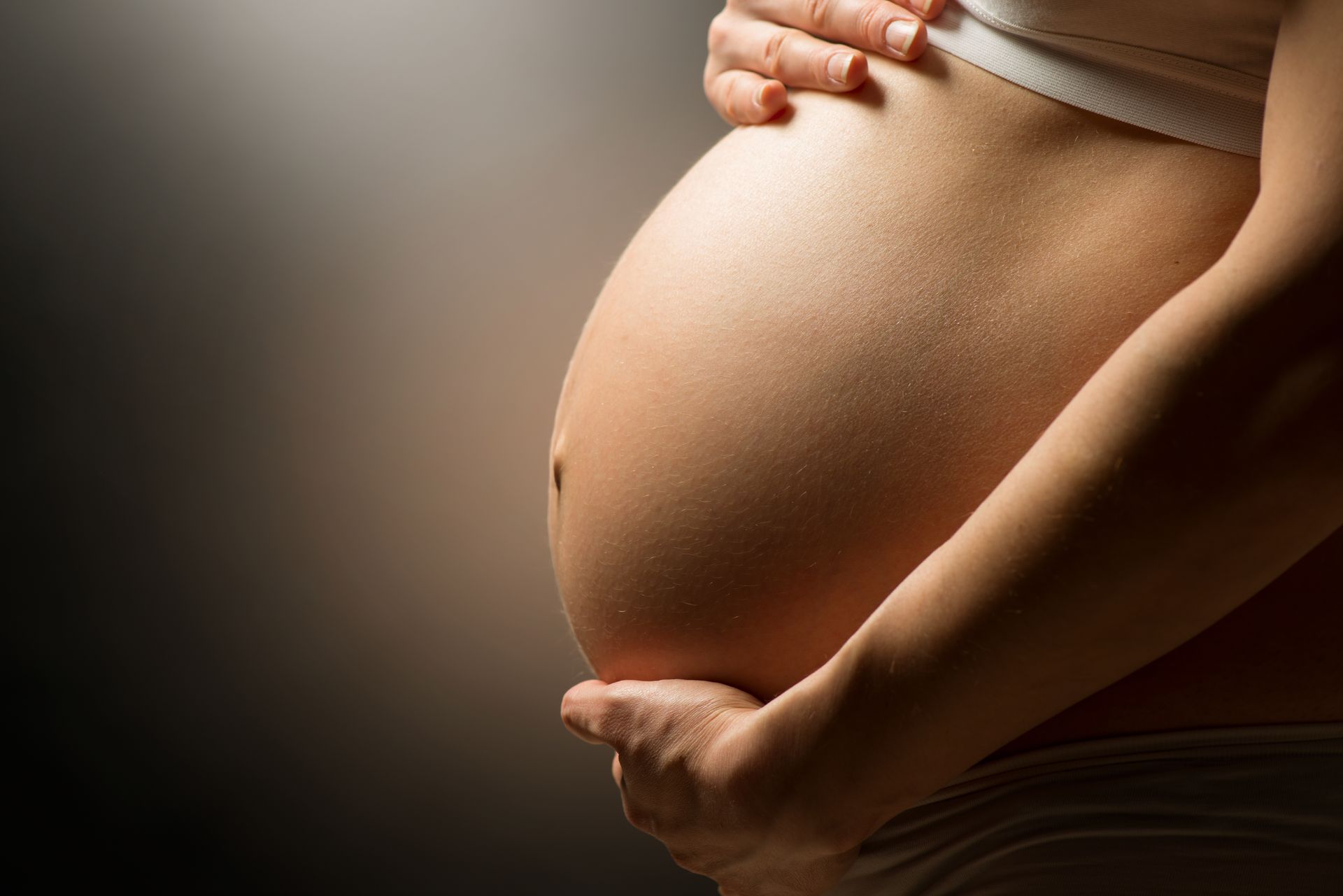 Pregnant belly with hands gently cradling it against a dark background