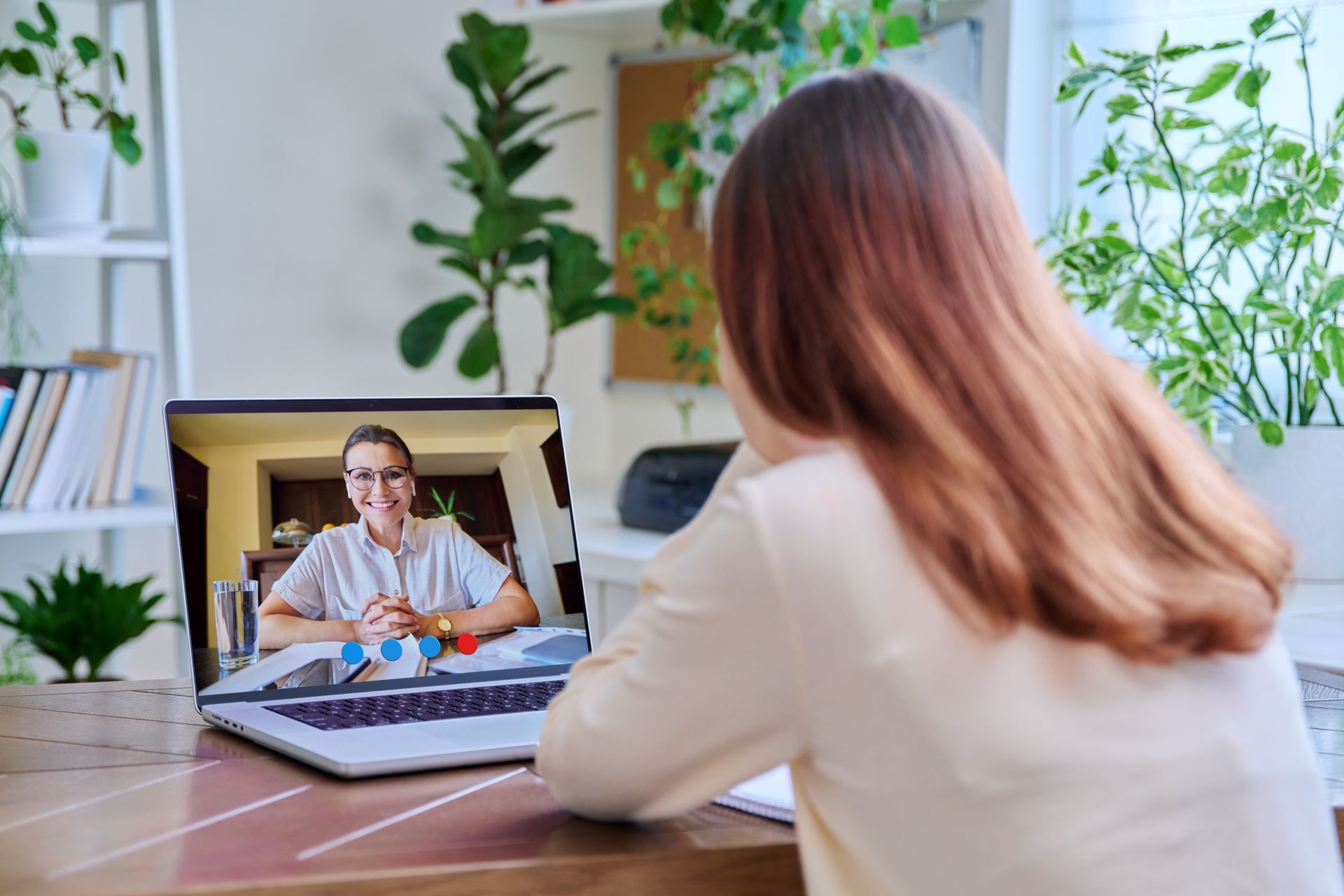 Woman video chatting with a doctor on a laptop in a bright home office