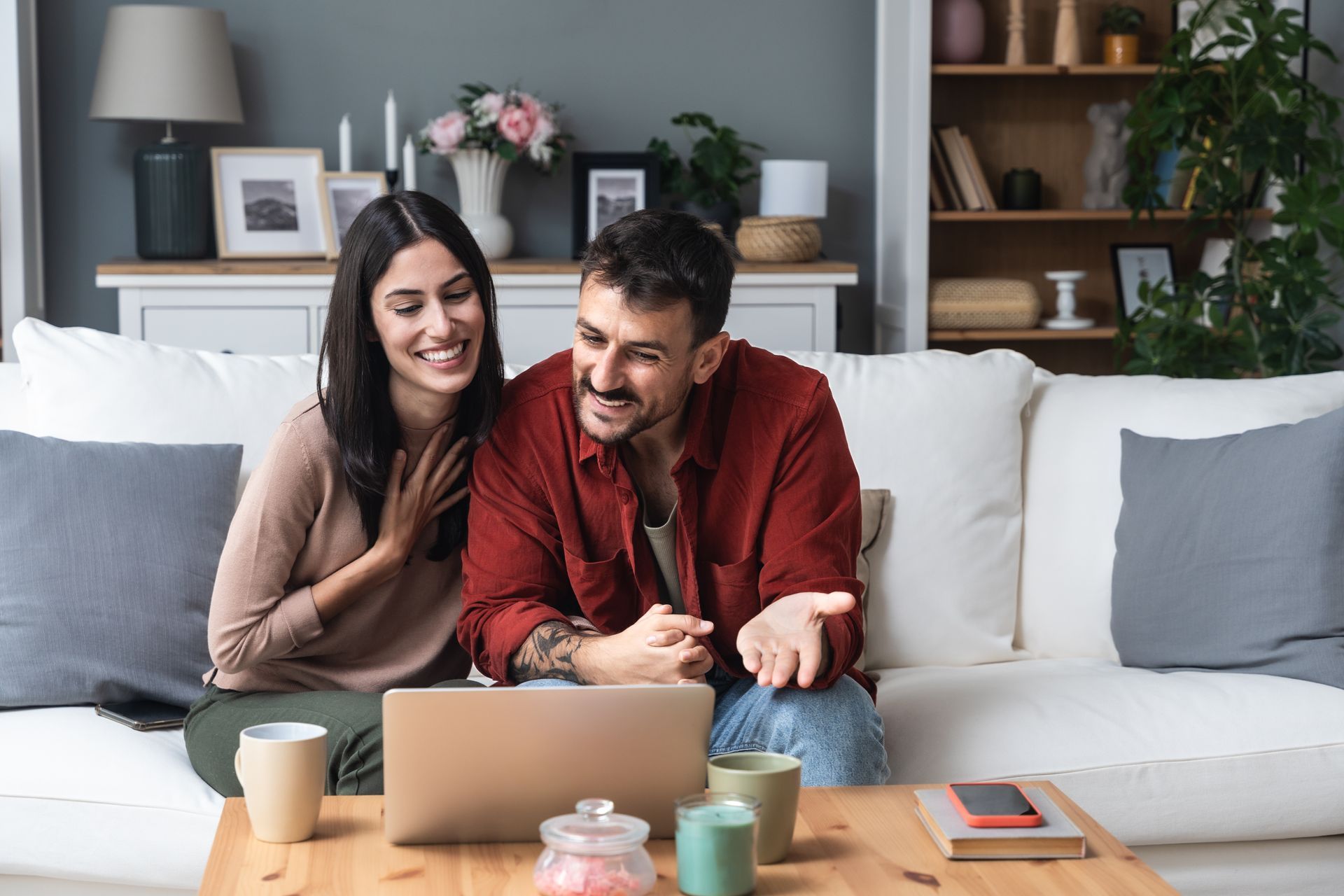Two people smiling on a couch with a laptop in a cozy living room
