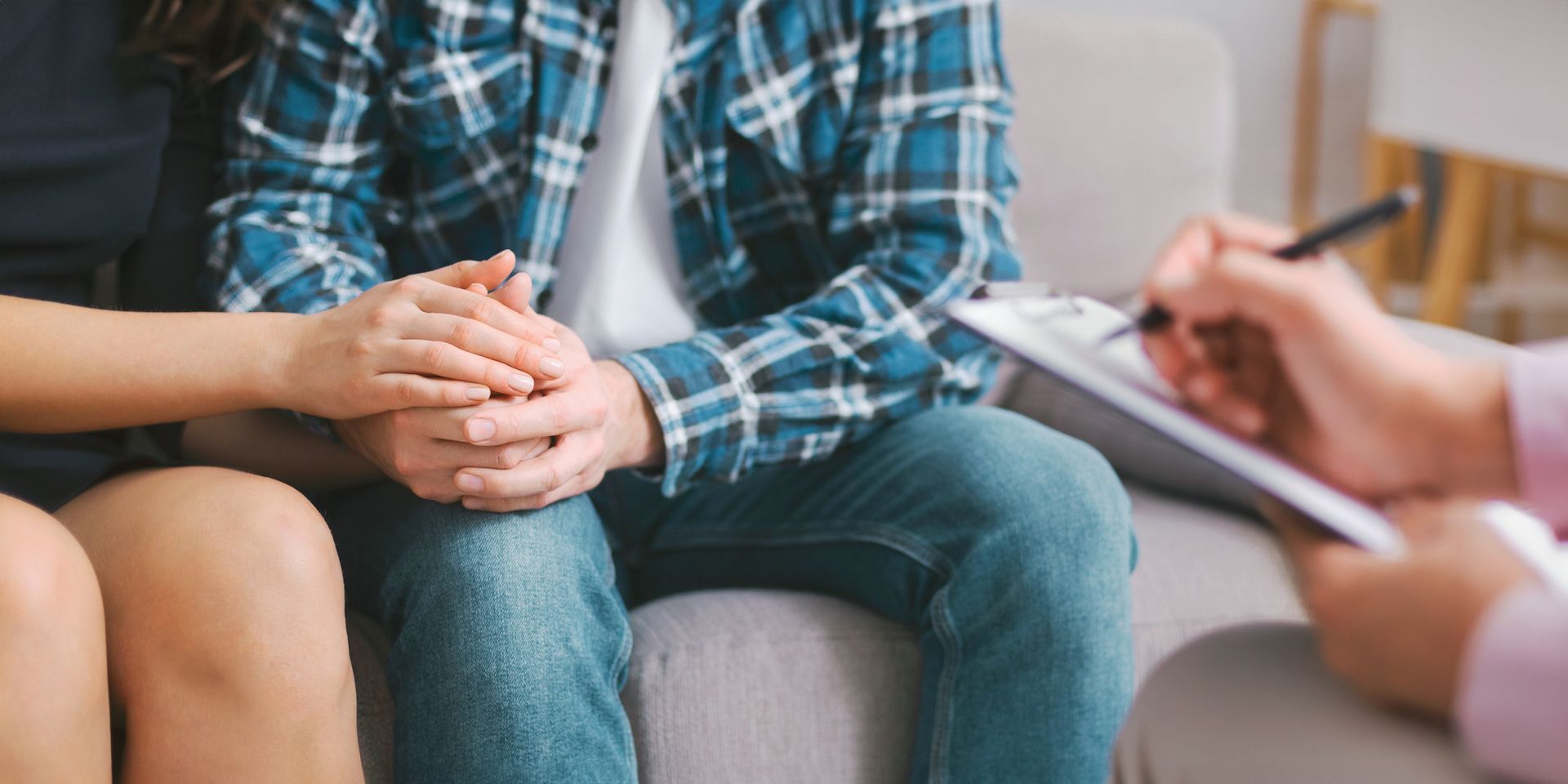 Three people in a counseling session, one taking notes while another sits with clasped hands.