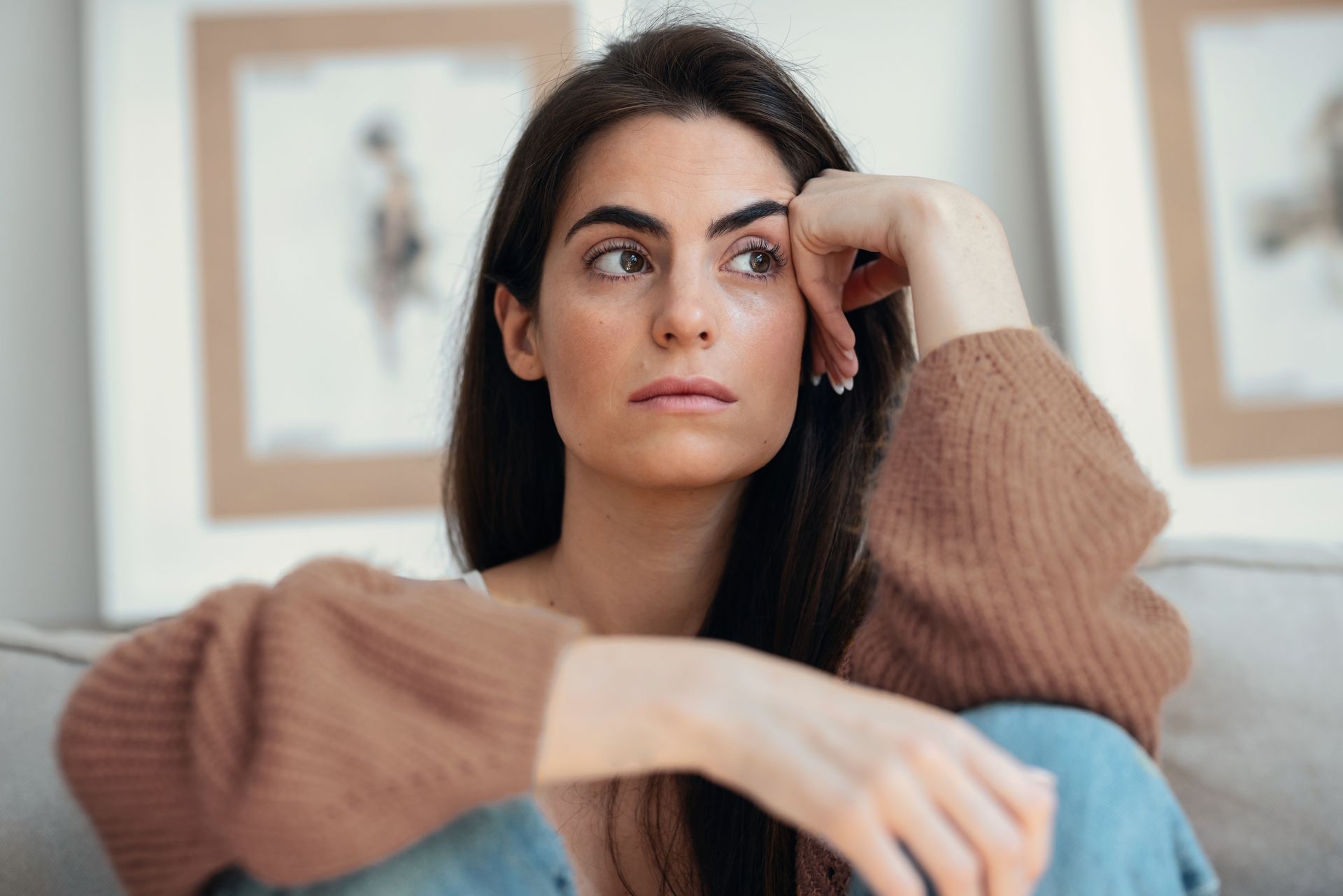 Woman sitting indoors with a pensive expression, resting her head on her hand.