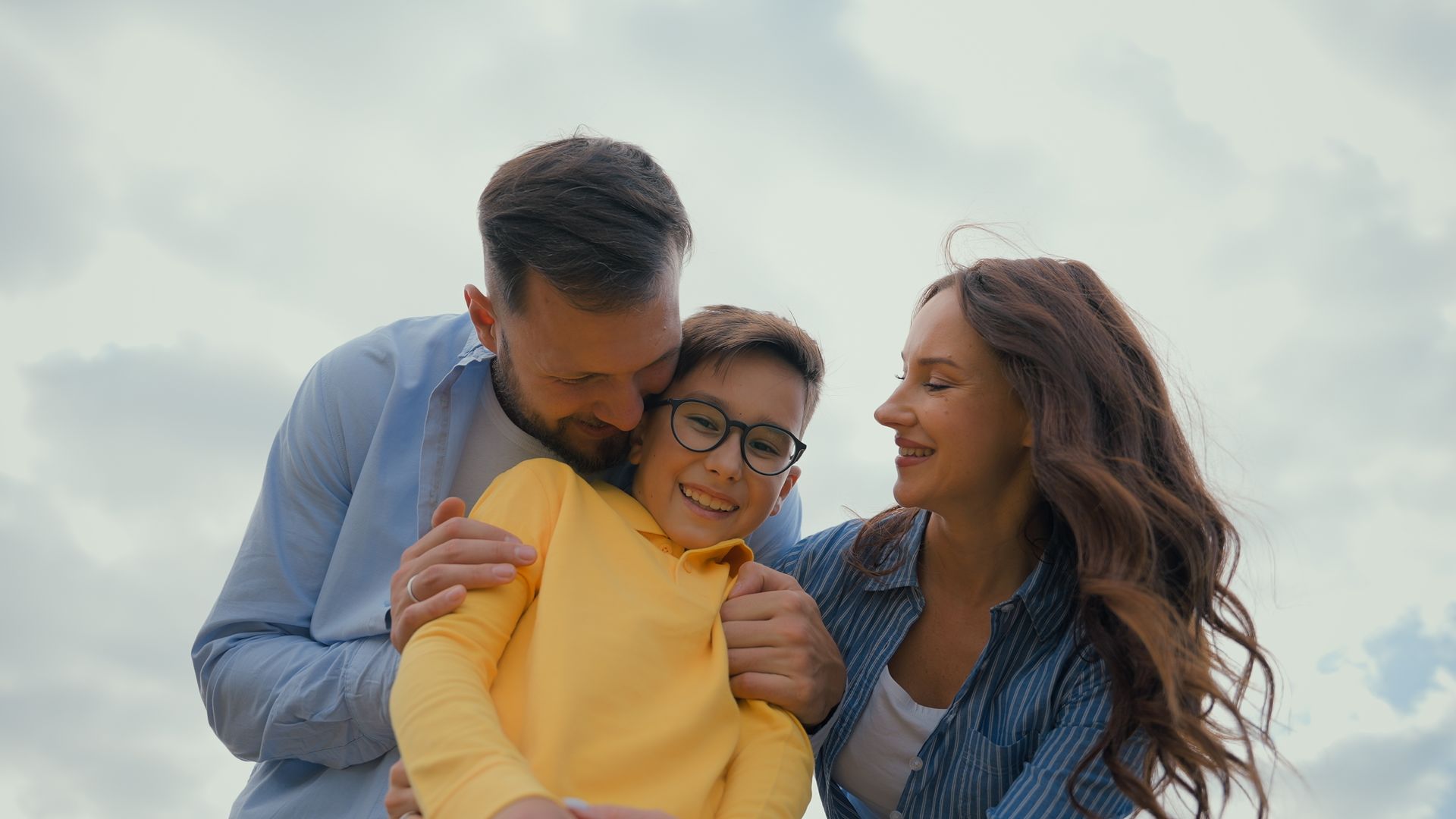 Three smiling people hugging outdoors against a cloudy sky