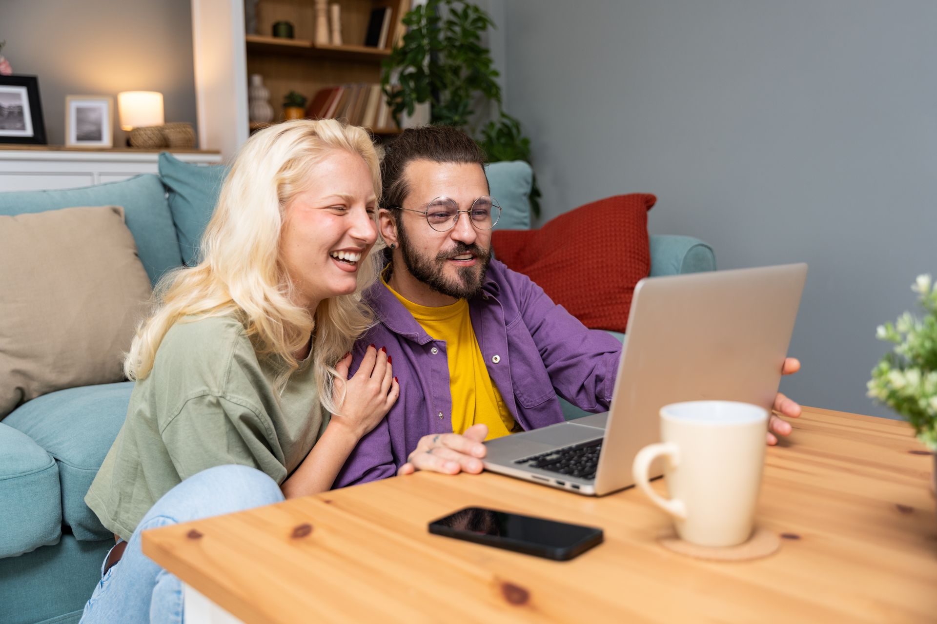 Two people smiling on a couch, looking at a laptop in a cozy living room
