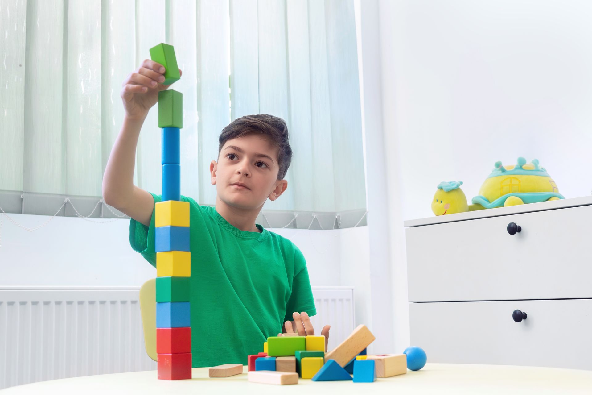 Child stacking colorful blocks at a table in a bright room