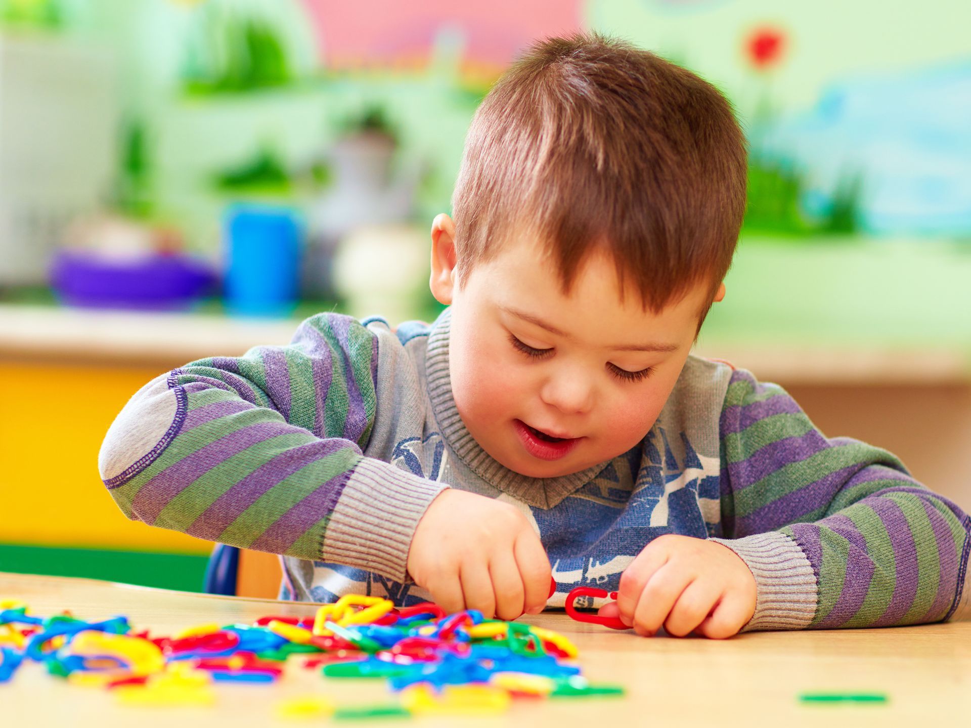Child playing with colorful blocks at a table, concentrating in a bright classroom.