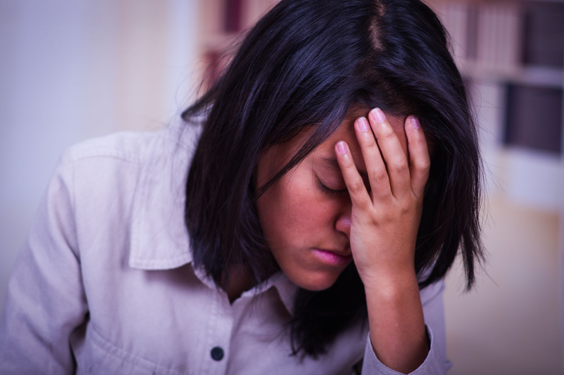 Person in a white shirt sitting with head in hand, looking distressed.