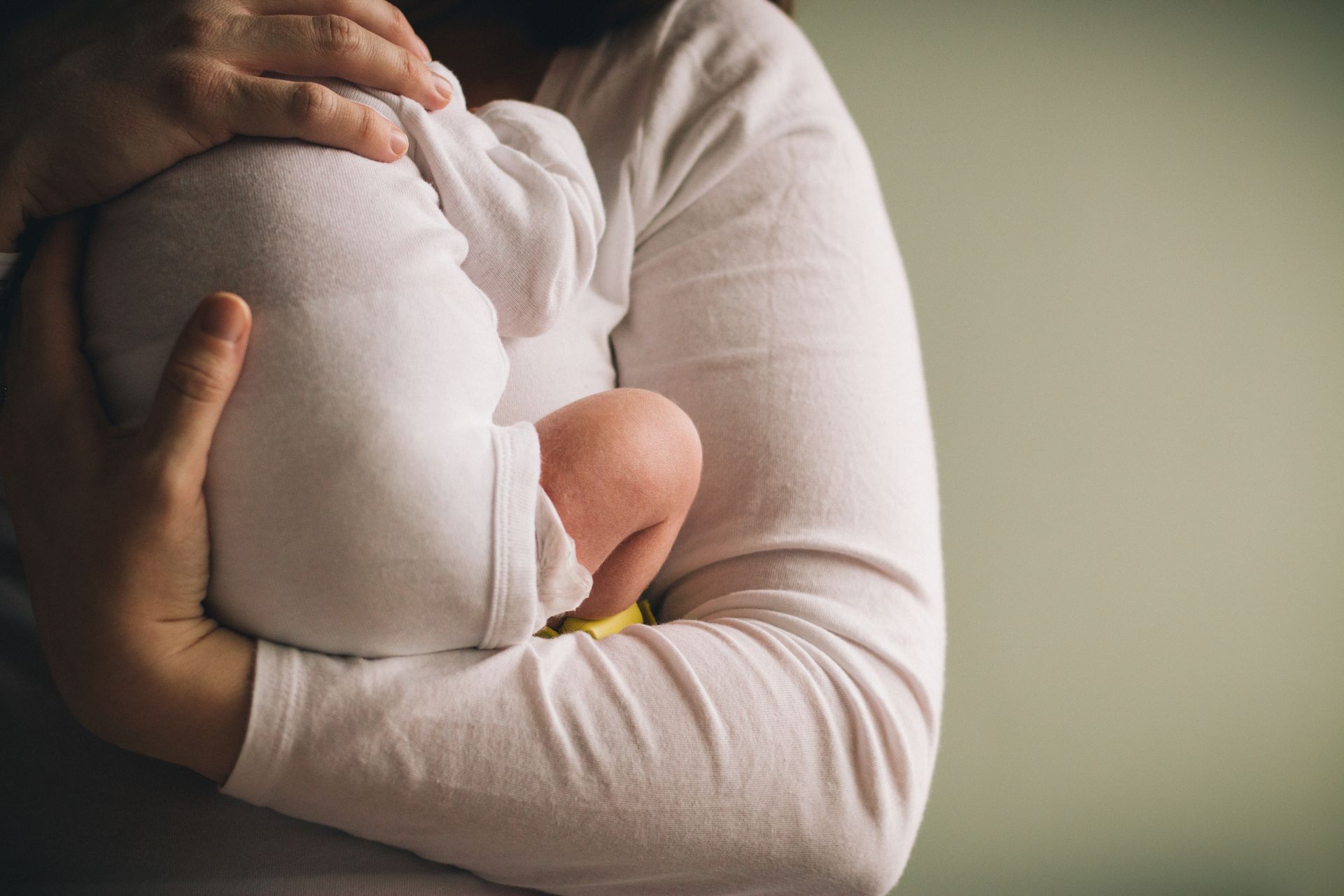 Person cradling a baby wrapped in a white blanket against their chest