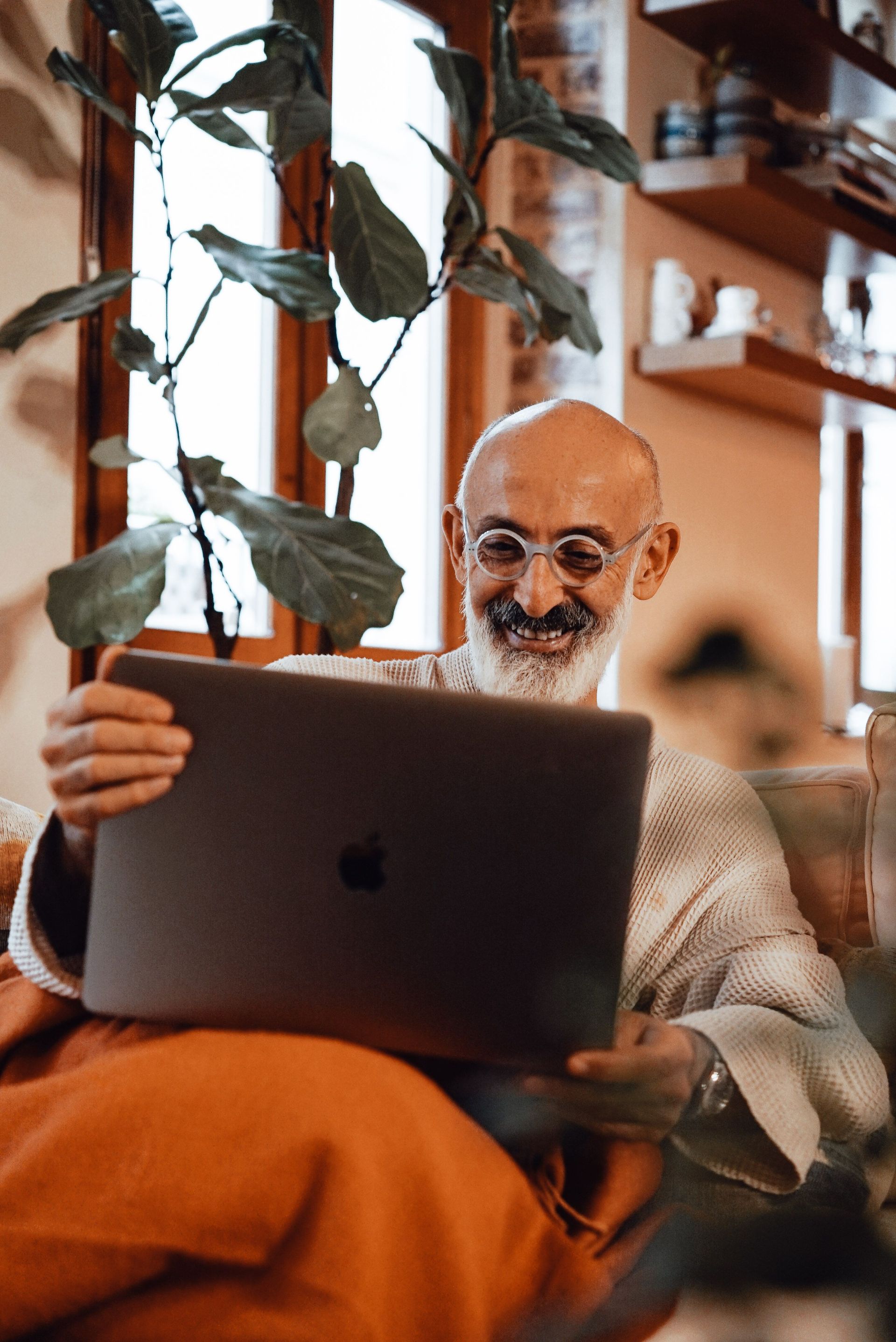 Man sitting on a couch, clutching his chest while looking at a laptop in a bright living room