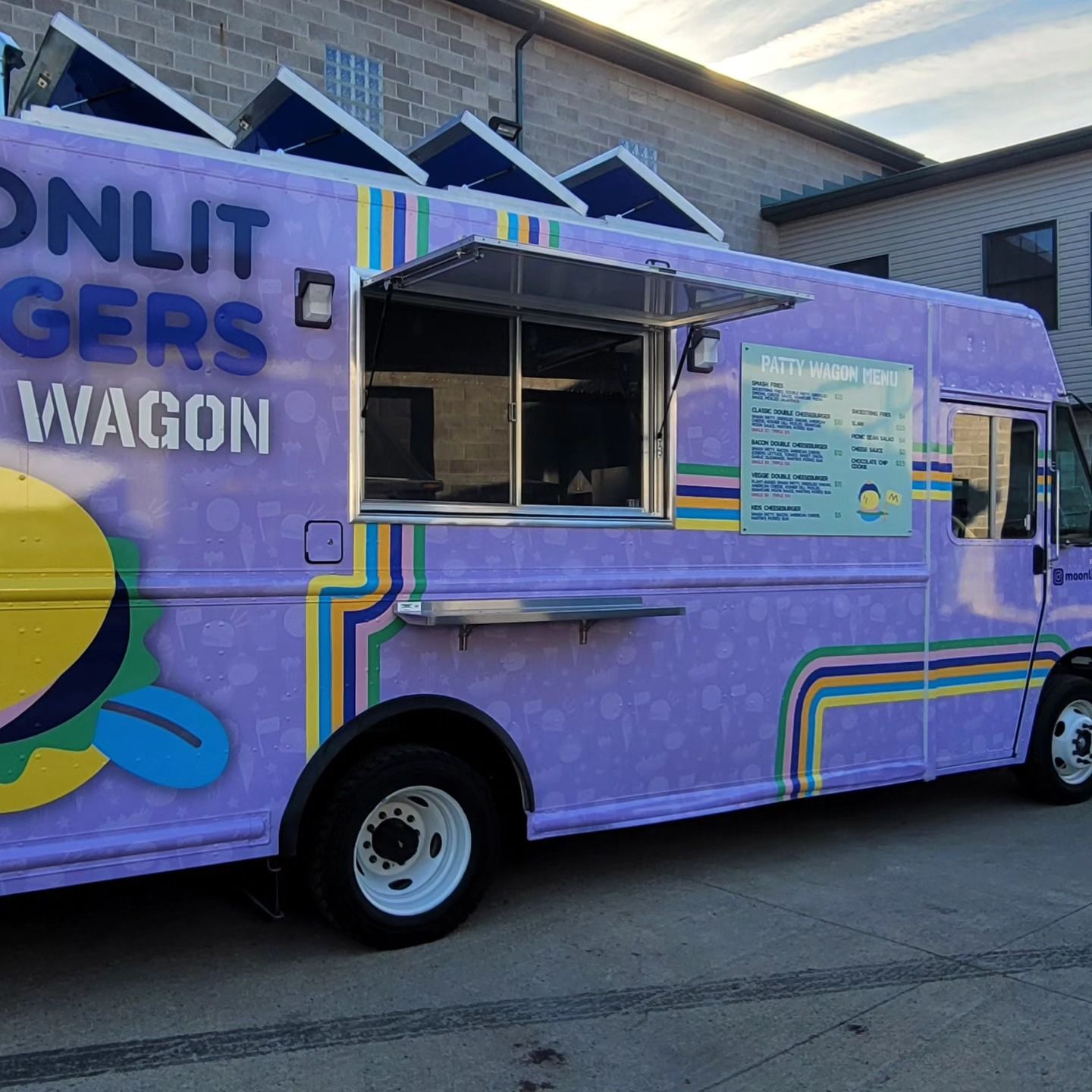 Purple food truck with a serving window open, parked outside a building.
