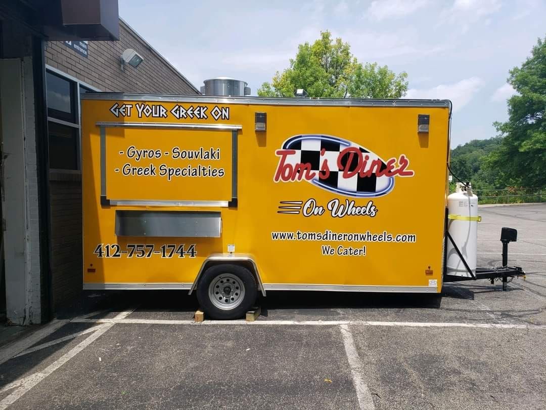 Yellow Tom's Diner food truck with a checkered logo, serving sandwiches and specialties, parked outside.