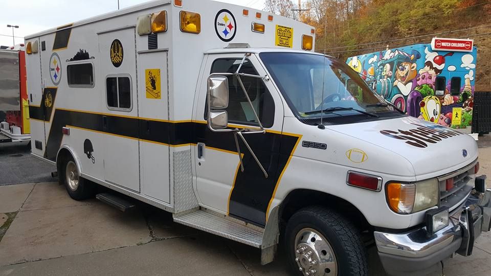 White ambulance with black and yellow accents, Steelers logo, parked near a colorful mural.
