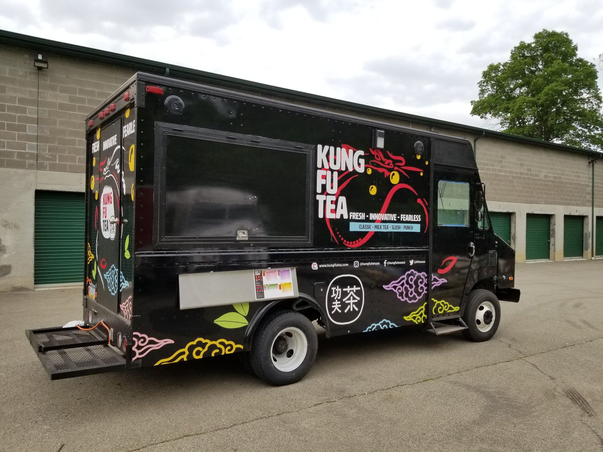 Black Kung Fu Tea food truck with colorful graphics parked near storage units.