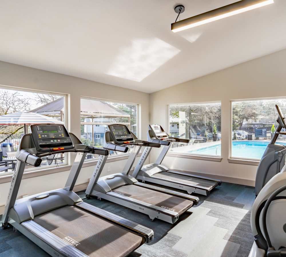 Treadmills in a gym with windows overlooking a pool and patio.
