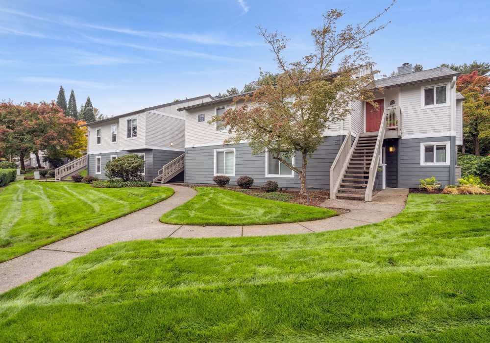 Two-story apartment building with green lawn, walkways, and stairs leading to entrances. Gray and white exterior.