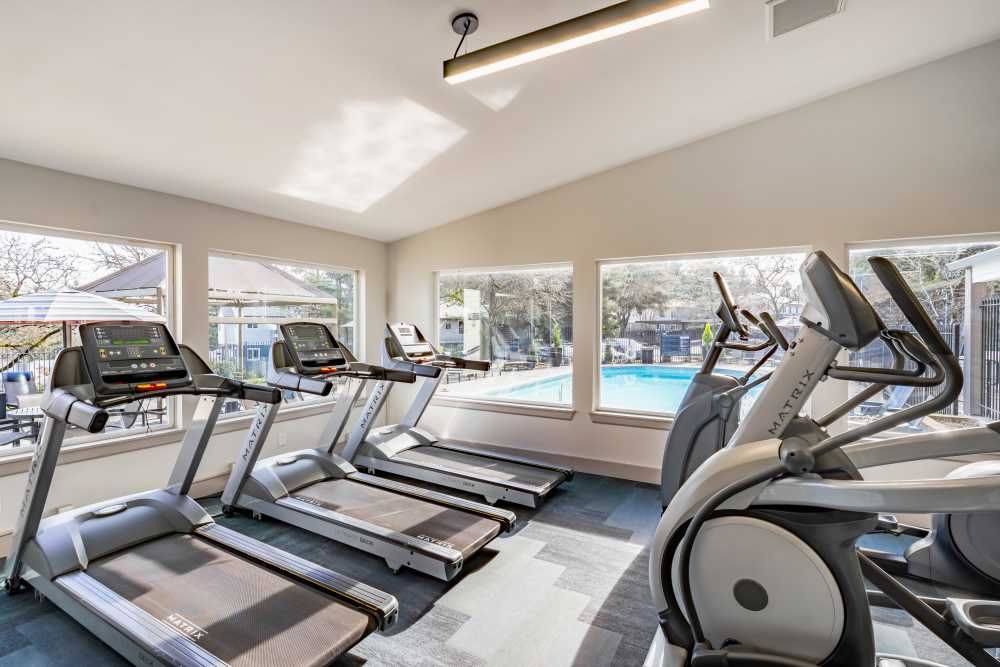 Indoor fitness center with treadmills and ellipticals by large windows overlooking a pool.