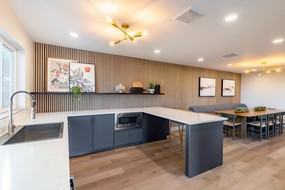 Modern communal kitchen with island, sink, and long dining table in a clubhouse.