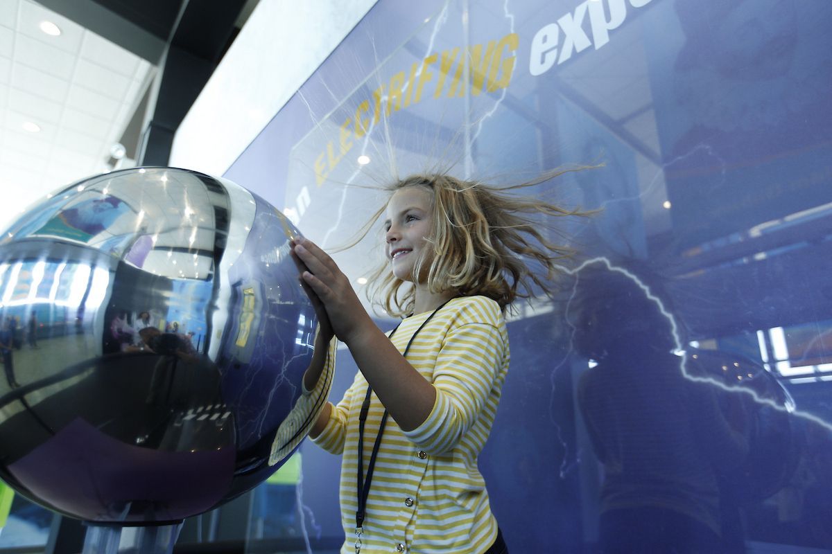 A young girl is playing with a sphere in a museum.