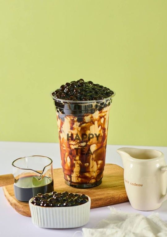 Iced coffee with chocolate drizzle and coffee beans on a wooden board beside a milk pitcher and syrups