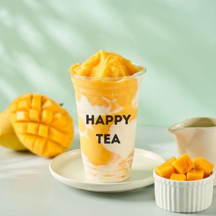 Mango tea drink in a clear cup labeled “HAPPY TEA,” with mango pieces on a light green background