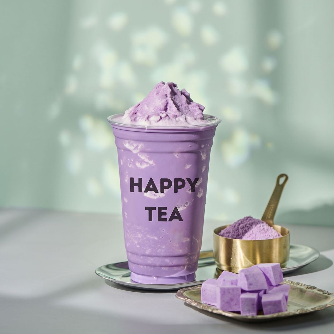 Purple “HAPPY TEA” drink in a clear cup, with matching lavender treats on plates.