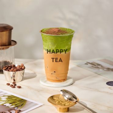Green and orange tea cup with “HAPPY TEA” text on a saucer on a tabletop.