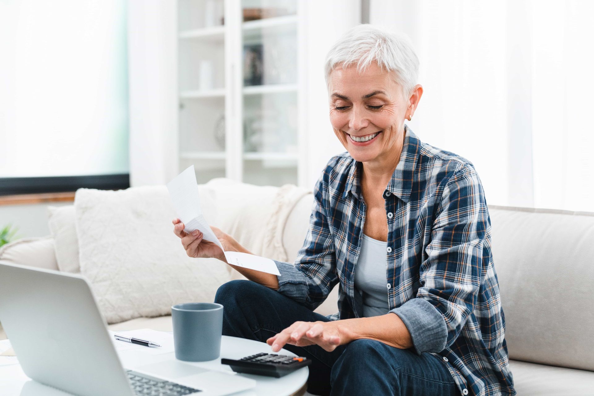 Woman calculates finances on a laptop and calculator, holding a bill.