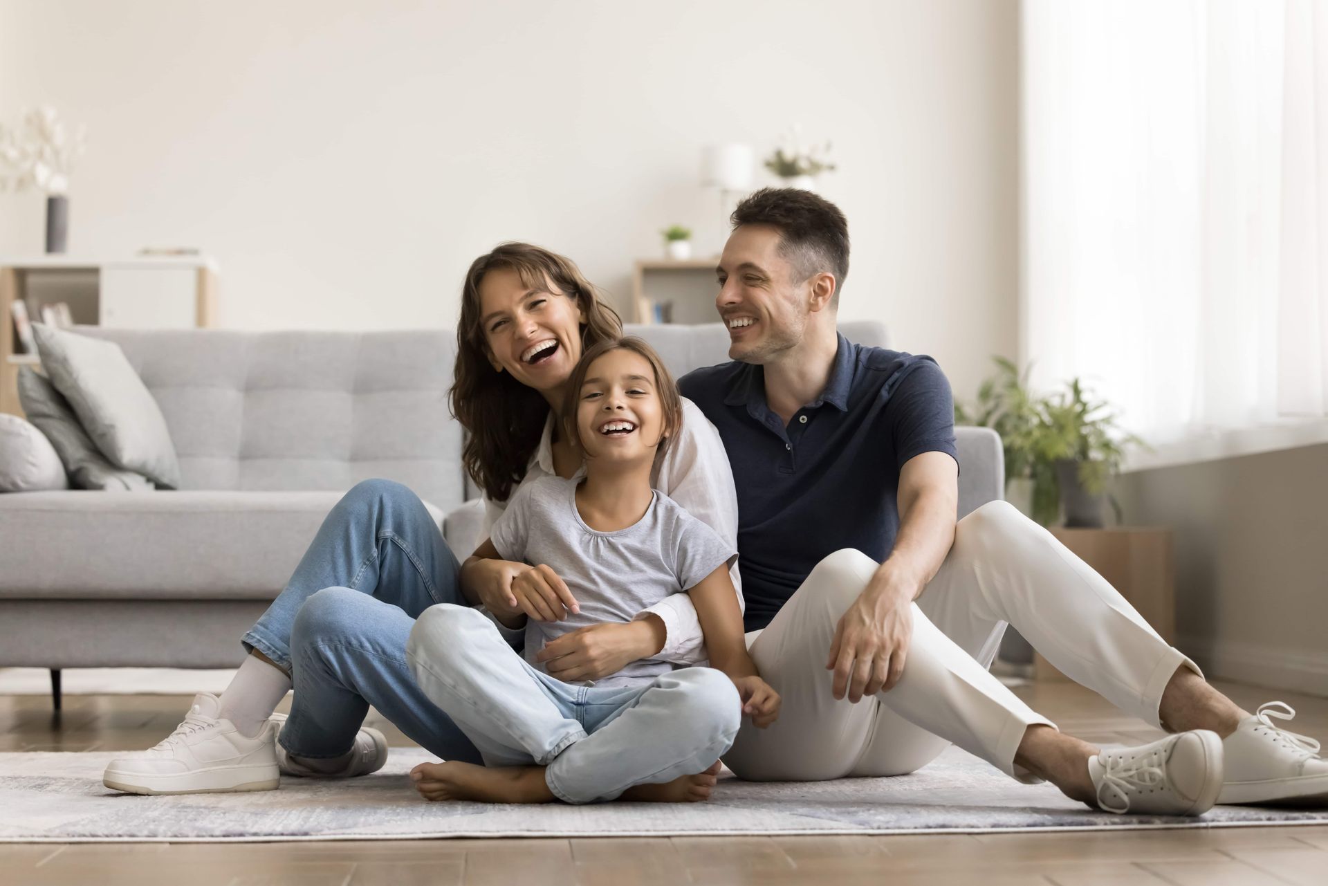 Family sitting on the floor laughing. A sofa and plants are in the background.