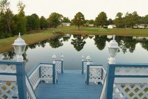 Blue deck overlooking a calm pond with trees and white lantern posts at sunset