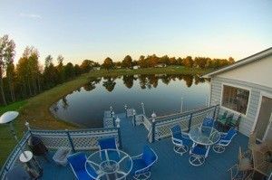 Patio with blue chairs overlooking a calm pond at sunset, surrounded by trees and a house
